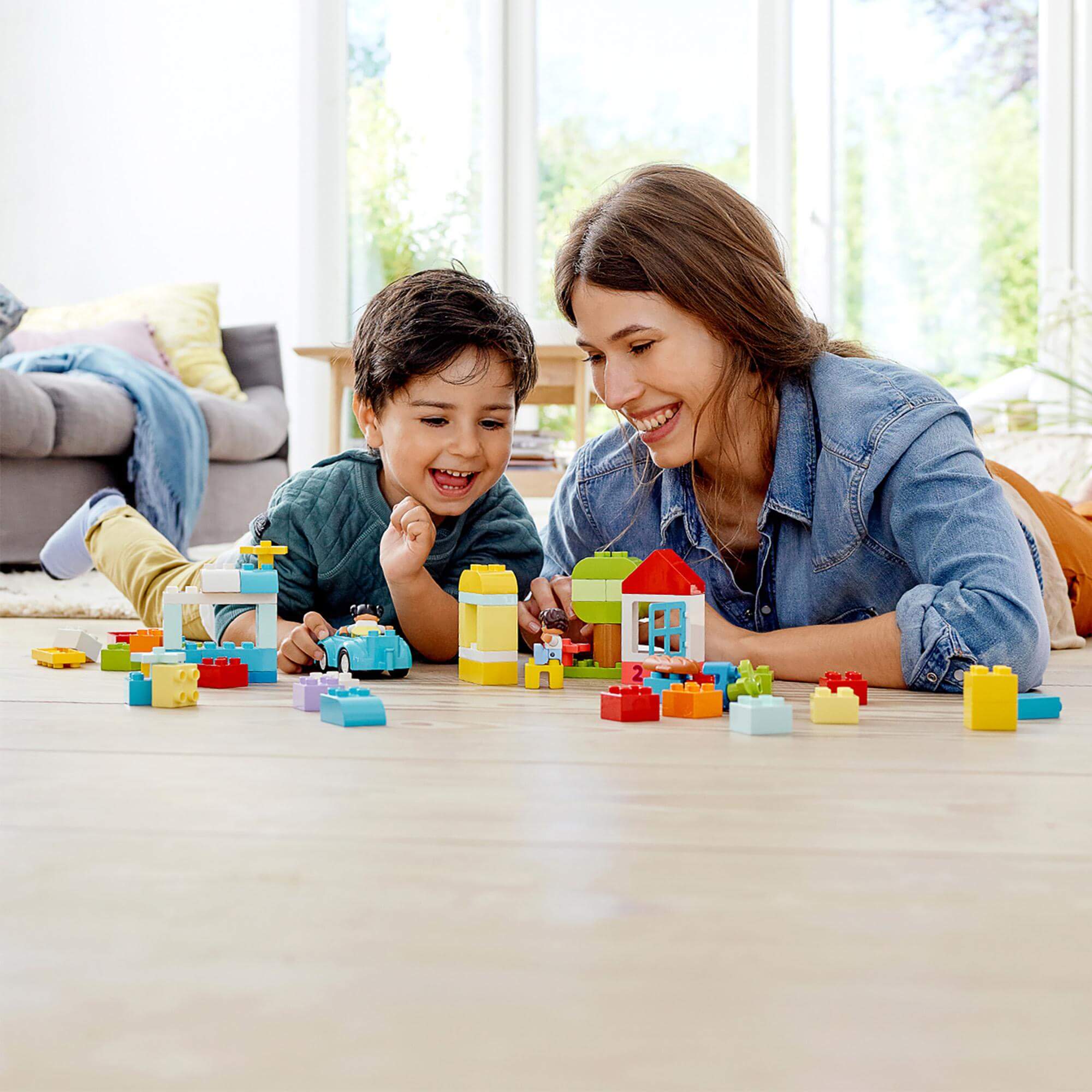 A happy child and parent playing together with LEGO® DUPLO bricks on the floor, fostering creativity and fun.