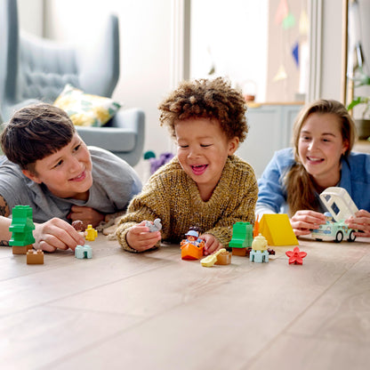 Child playing with LEGO® DUPLO family camping set alongside two adults, promoting fun and learning activities together.