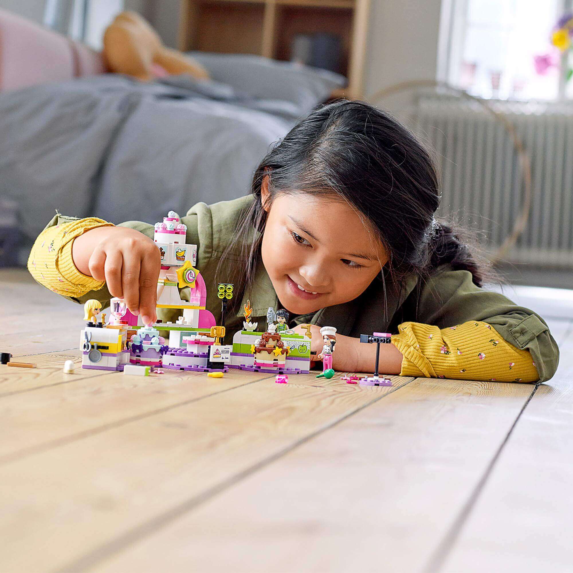 A girl joyfully playing with the LEGO® Friends Baking Competition Playset 41393, customizing colorful cakes in Heartlake City.