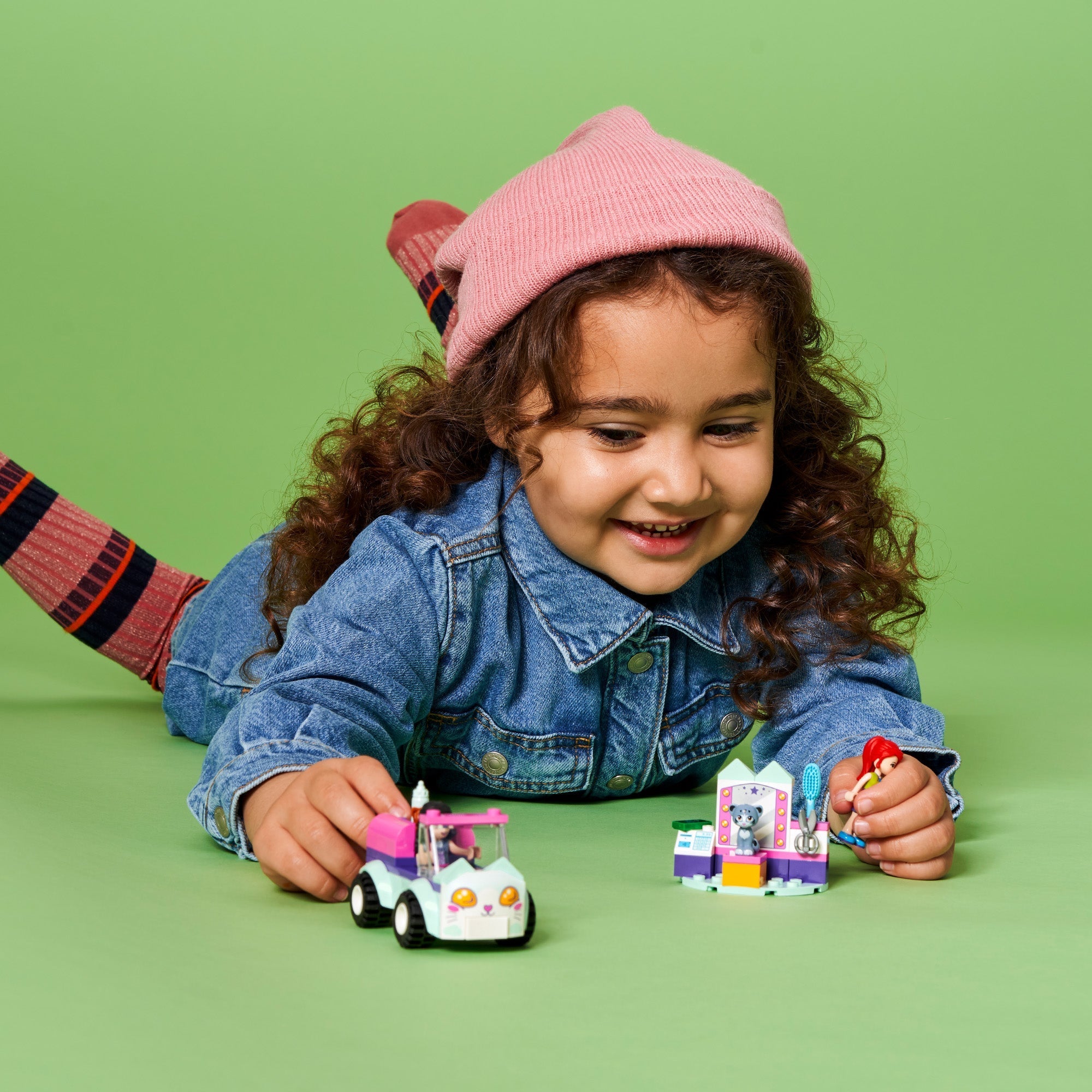Child playing with LEGO® Friends Cat Grooming Car set, featuring minidolls and cat figures on a green background.