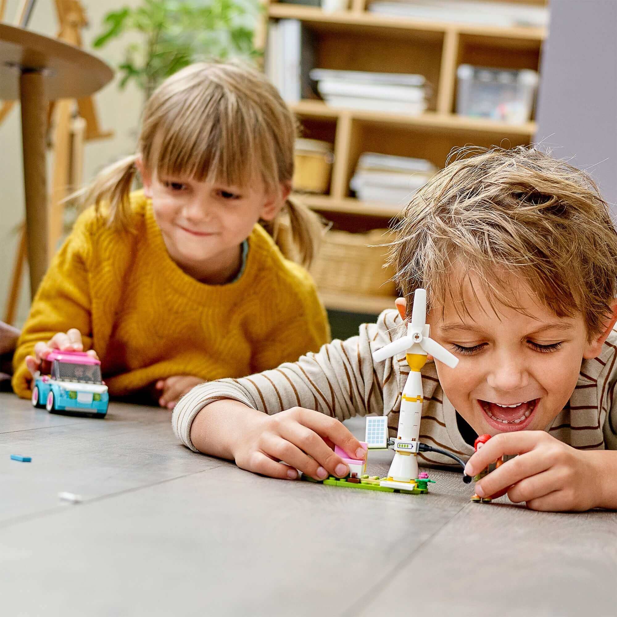 Two children playing with LEGO® Friends Olivia's Electric Car set, featuring a colorful car and wind turbine toy.