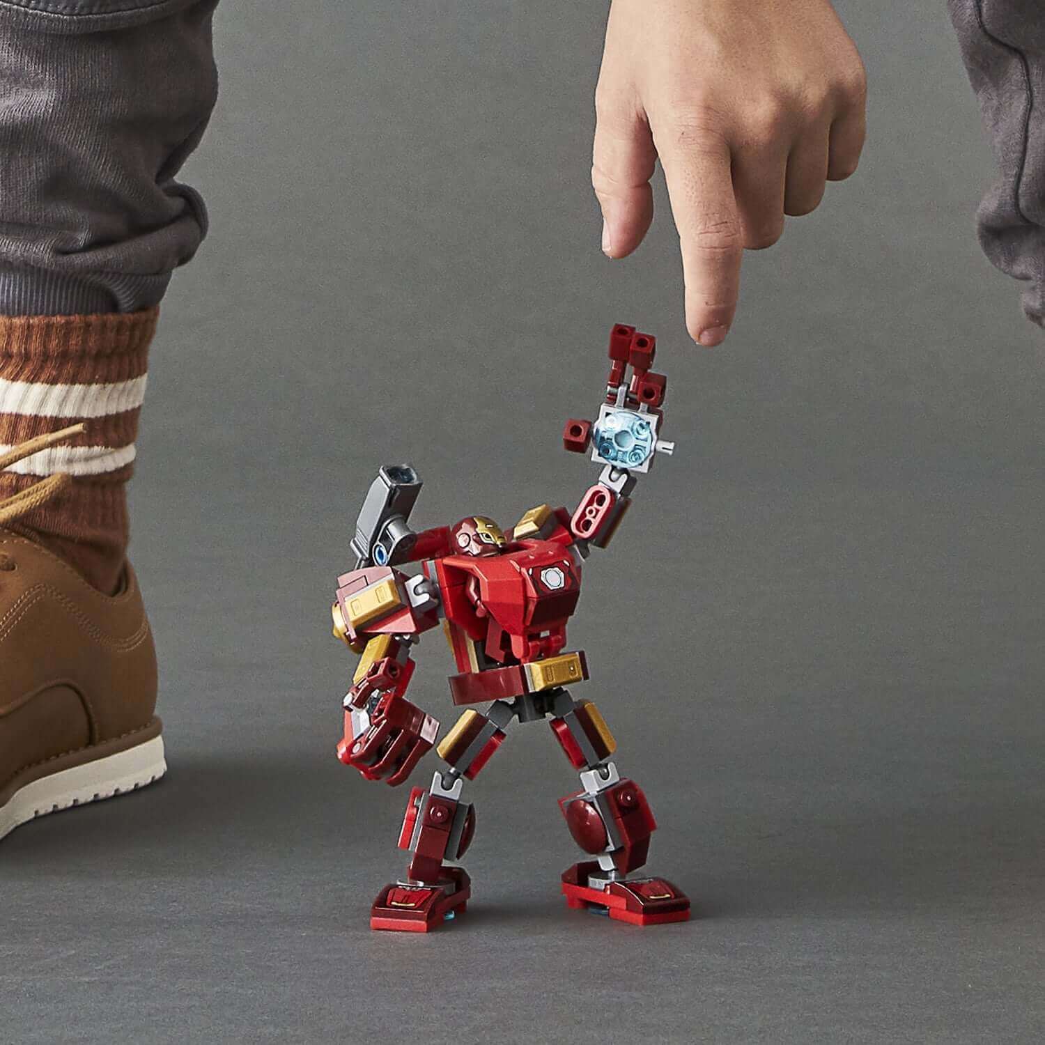 A child pointing at a LEGO® Iron Man mech playset, showcasing its detailed design and movable limbs.