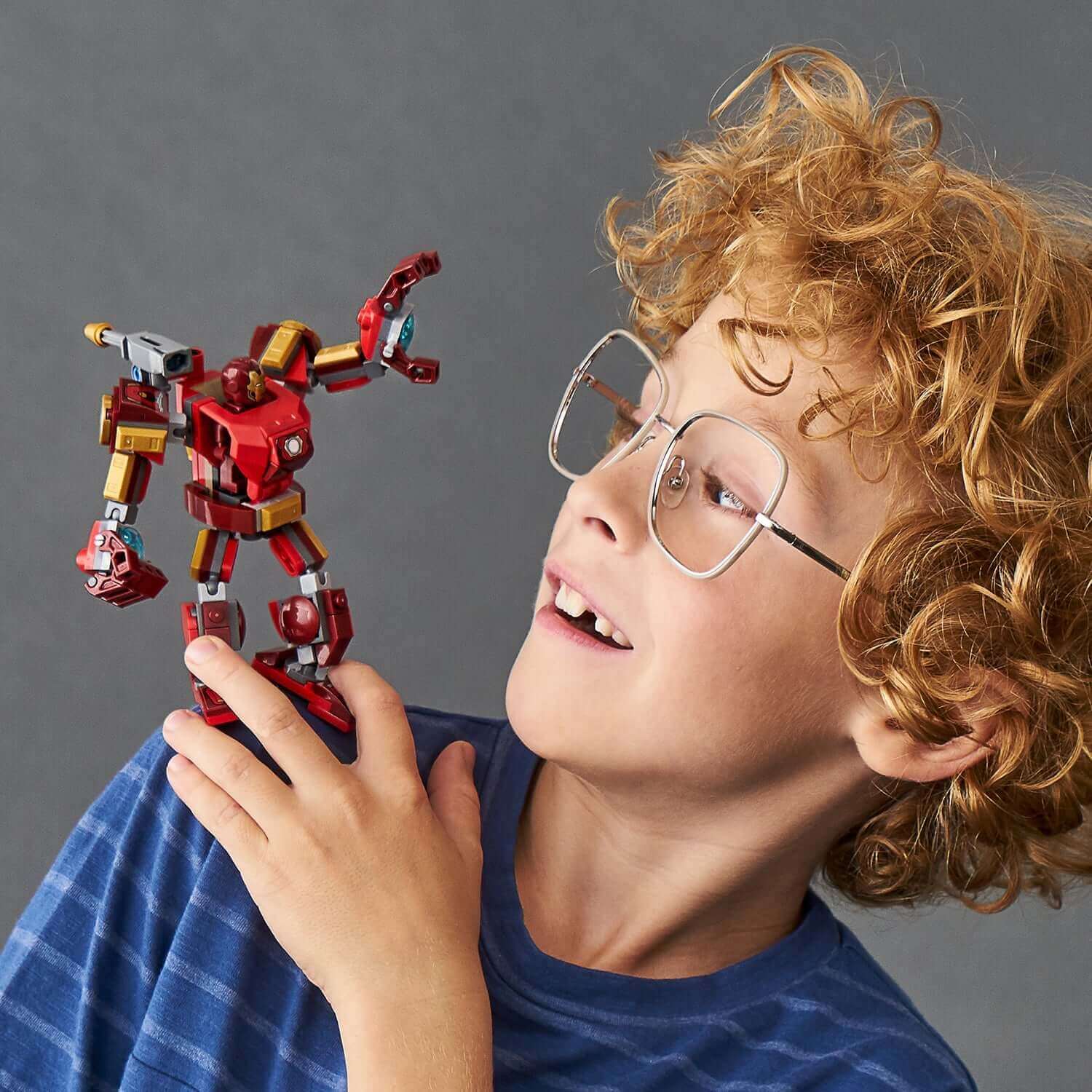 Child amazed by LEGO® Iron Man mech toy, showcasing creativity and playfulness in a vibrant setting.