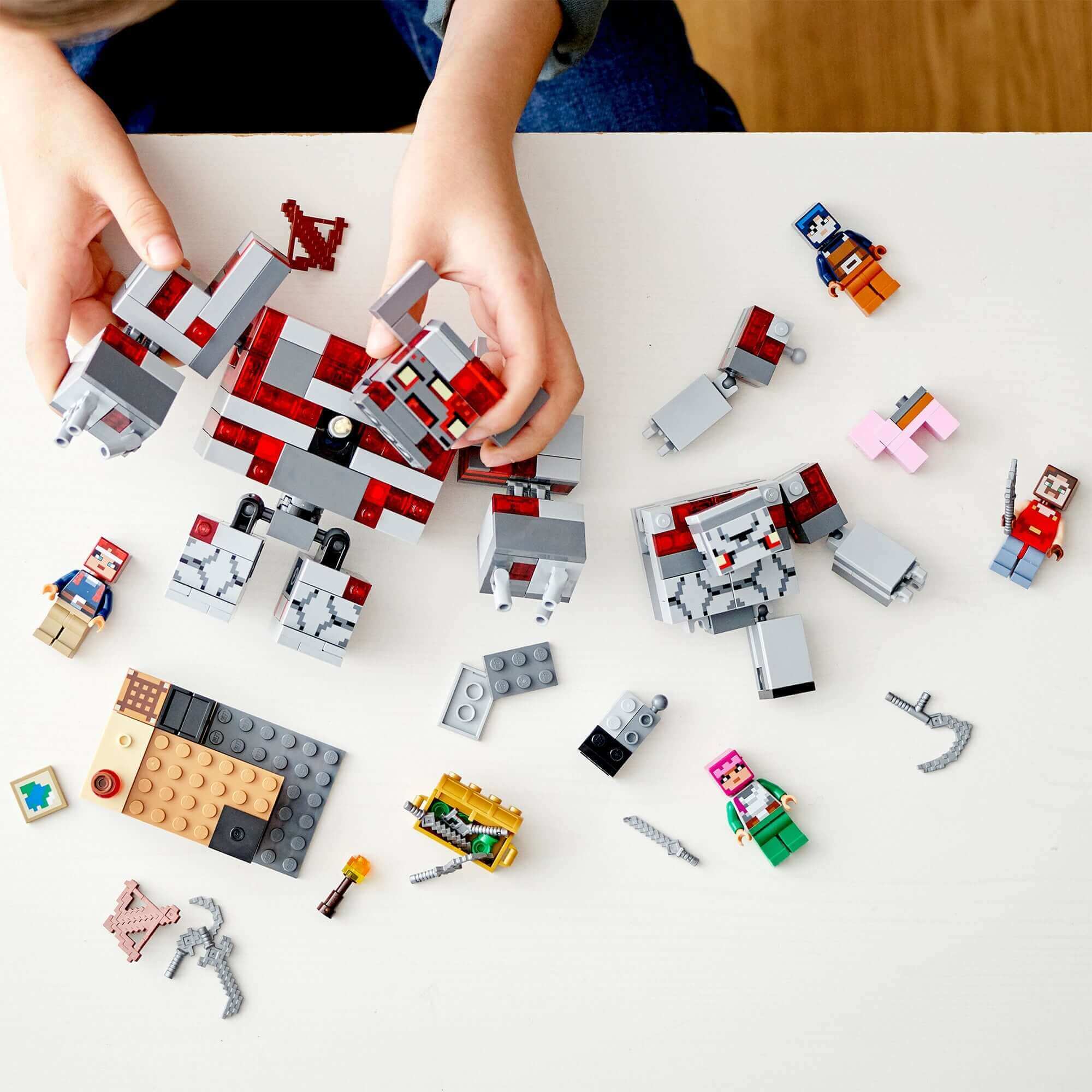 Child assembling LEGO Minecraft The Redstone Battle Set 21163 with characters and accessories on a table.