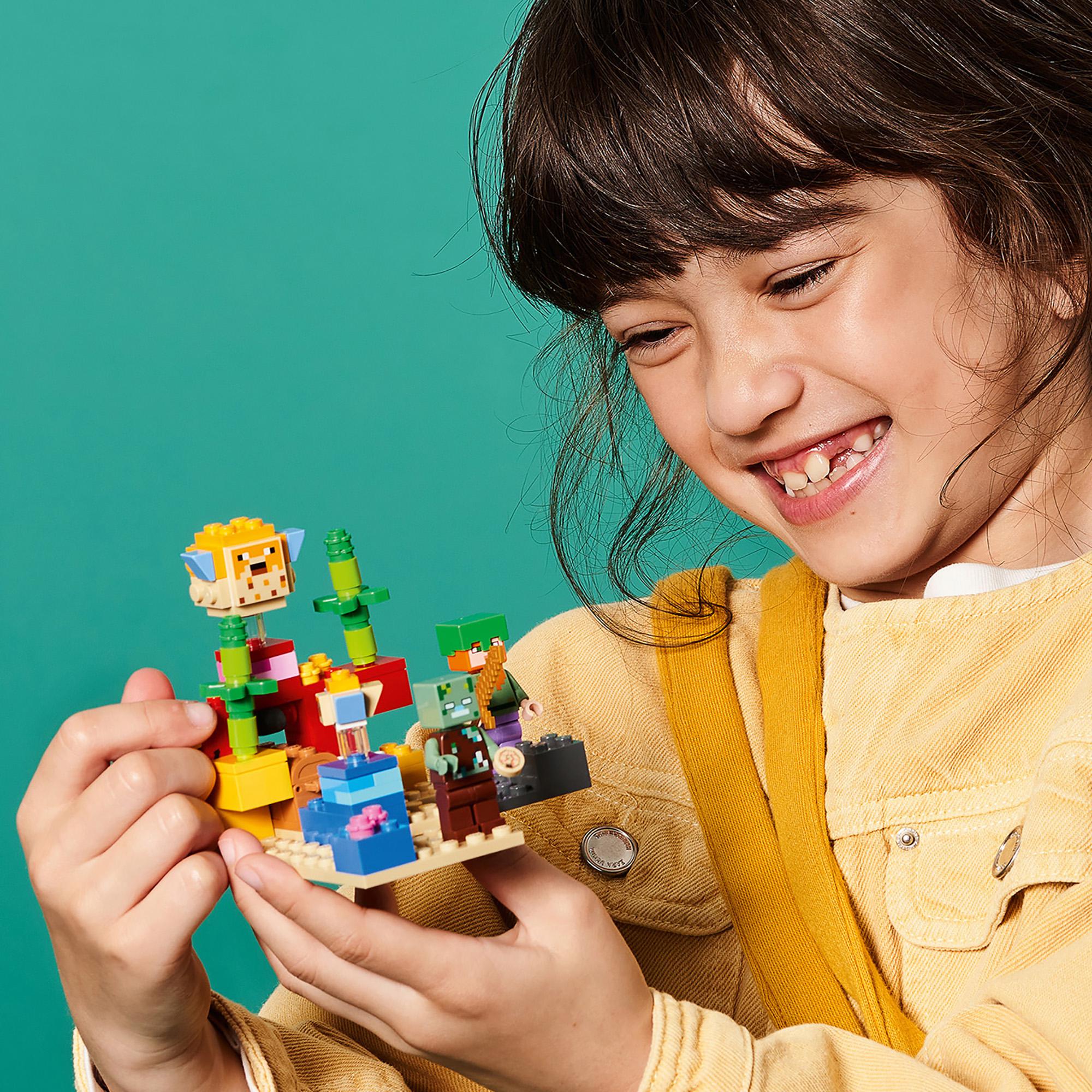 Child excitedly holding a colorful LEGO® Minecraft Coral Reef building set featuring underwater adventures.