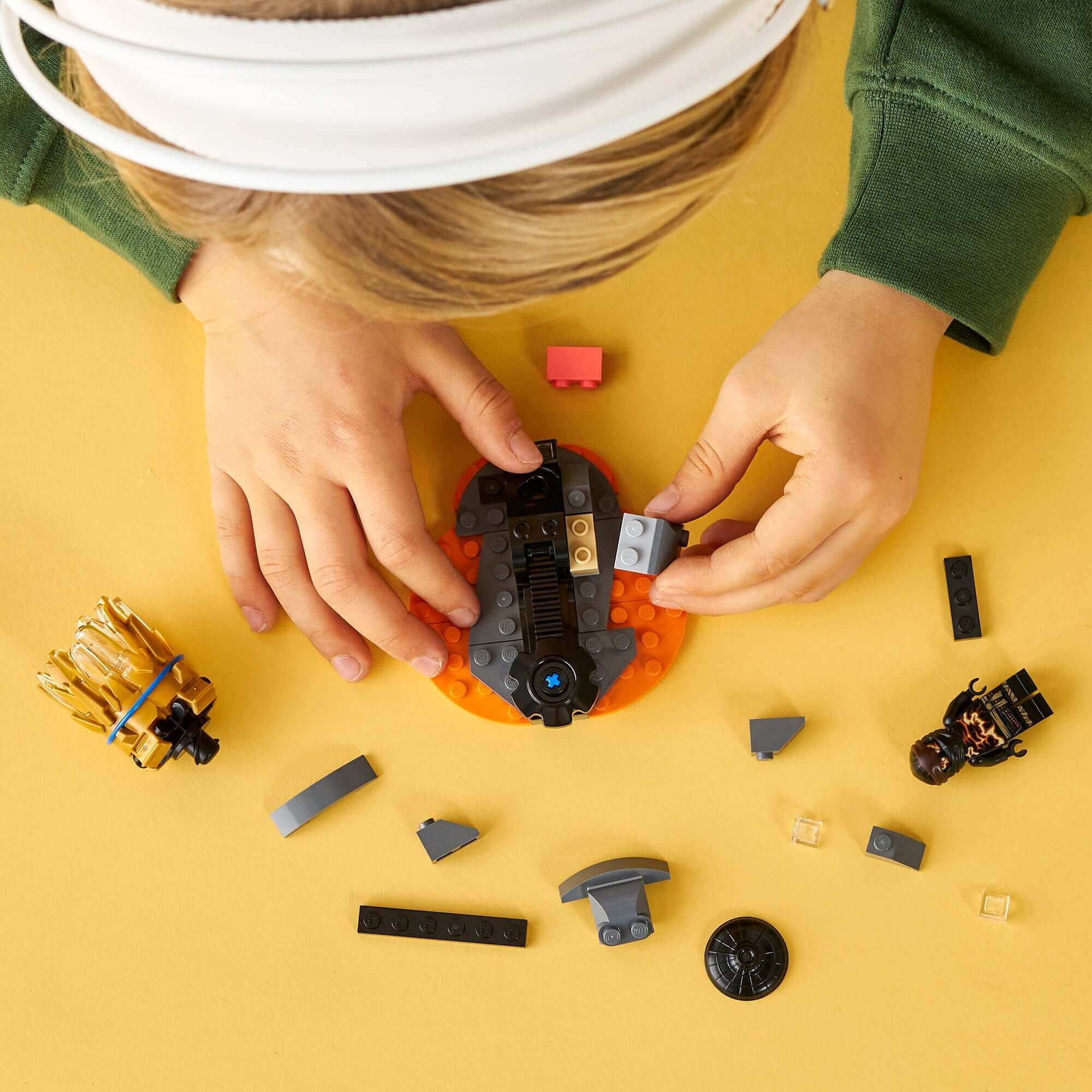 Child building with LEGO® NINJAGO Spinjitzu Burst Cole Spinner Toy 70685, surrounded by colorful pieces.