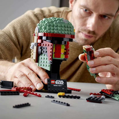 Adult builder assembling LEGO® Star Wars Boba Fett Helmet 75277 with colorful bricks and pieces, showcasing intricate details.