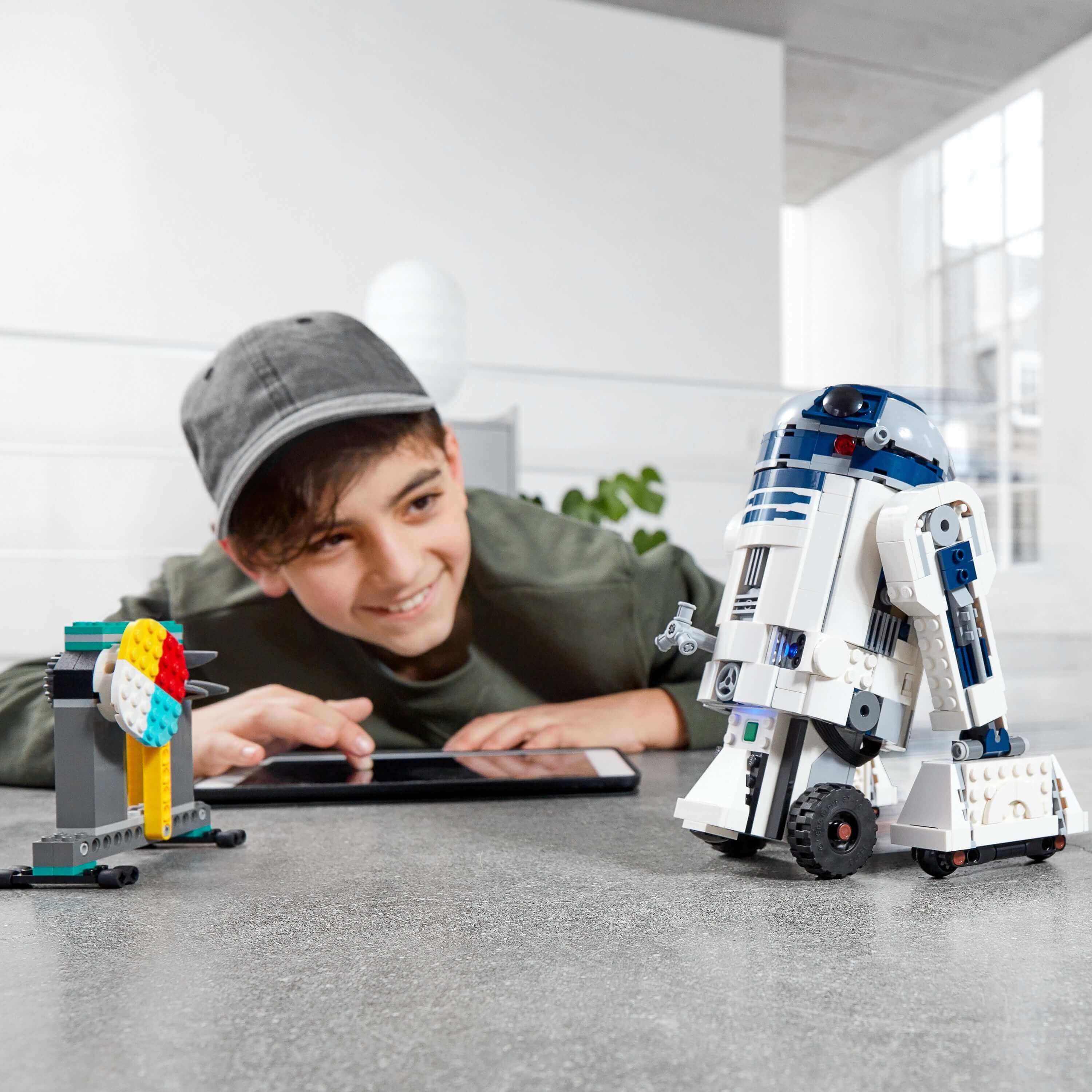 Child interacting with LEGO Star Wars BOOST Droid Commander R2-D2 and colorful buildable droid on a tablet.