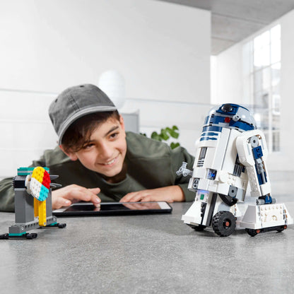 Child interacting with LEGO Star Wars BOOST Droid Commander R2-D2 and colorful buildable droid on a tablet.