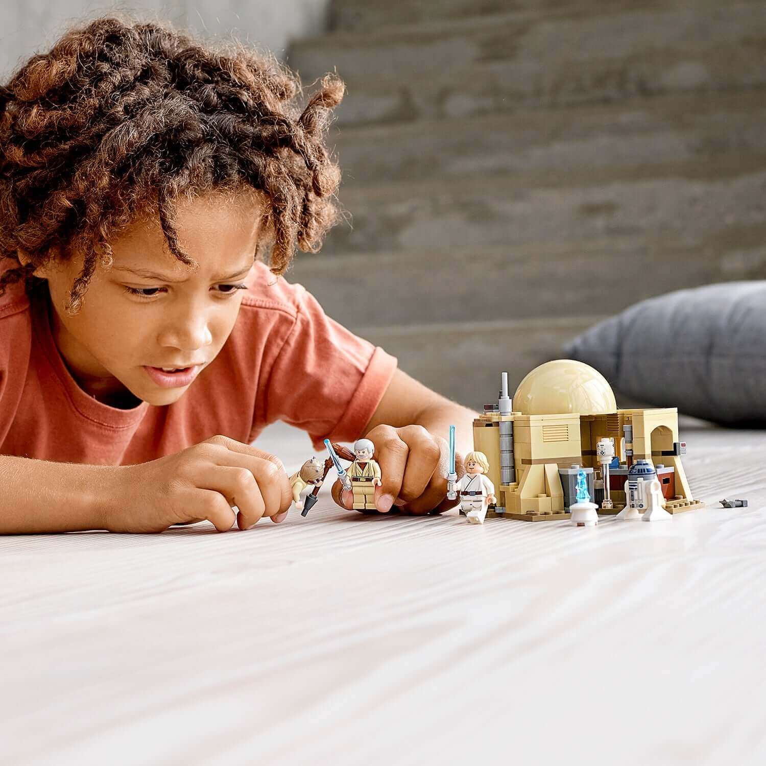 Child playing with LEGO Star Wars Obi-Wan's Hut 75270 featuring minifigures and accessories on a wooden floor.