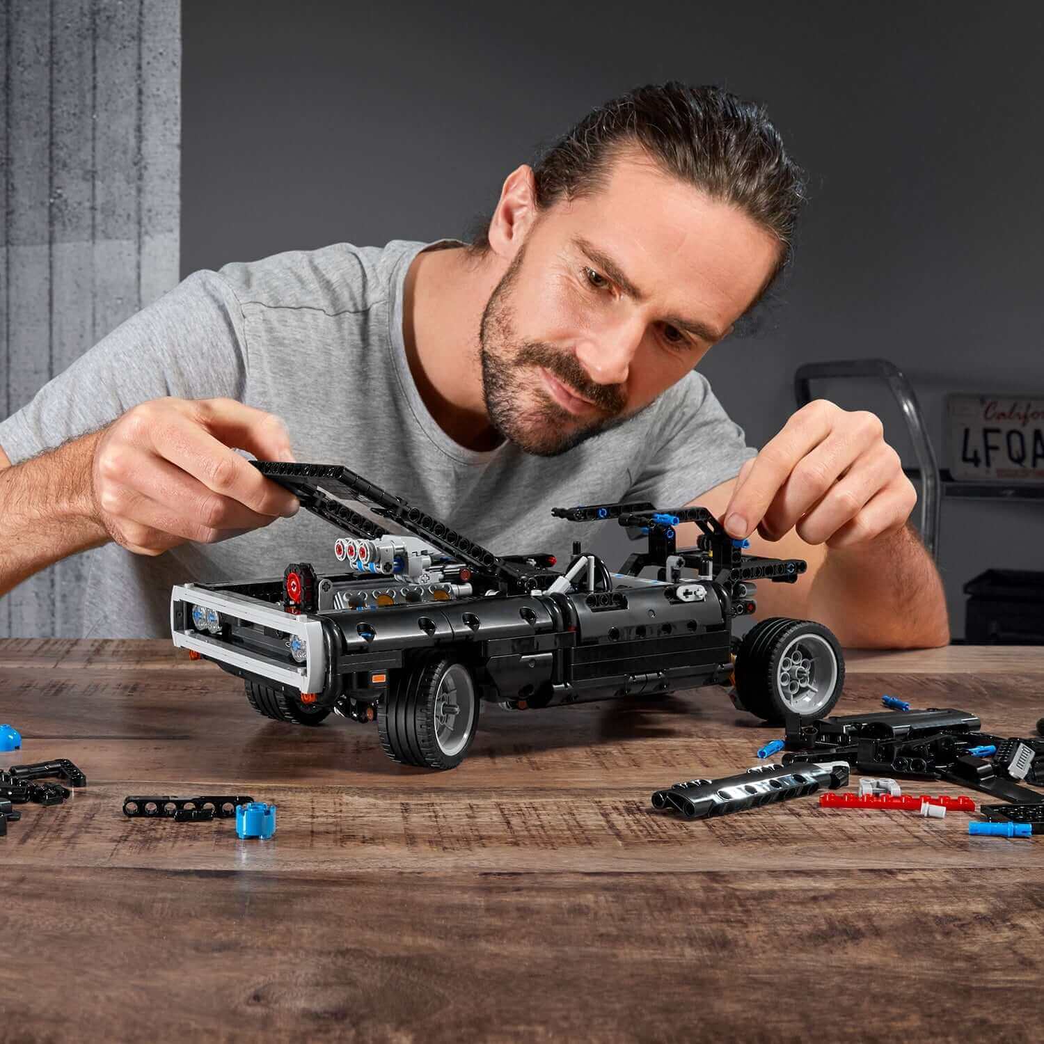 Person assembling LEGO® Technic Dom’s Dodge Charger from F&F set 42111 with building pieces on table.