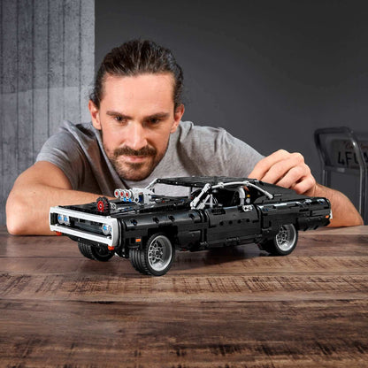 Man showcasing LEGO® Technic Dom's Dodge Charger F&F Set 42111 on a wooden table, inspired by The Fast and The Furious.