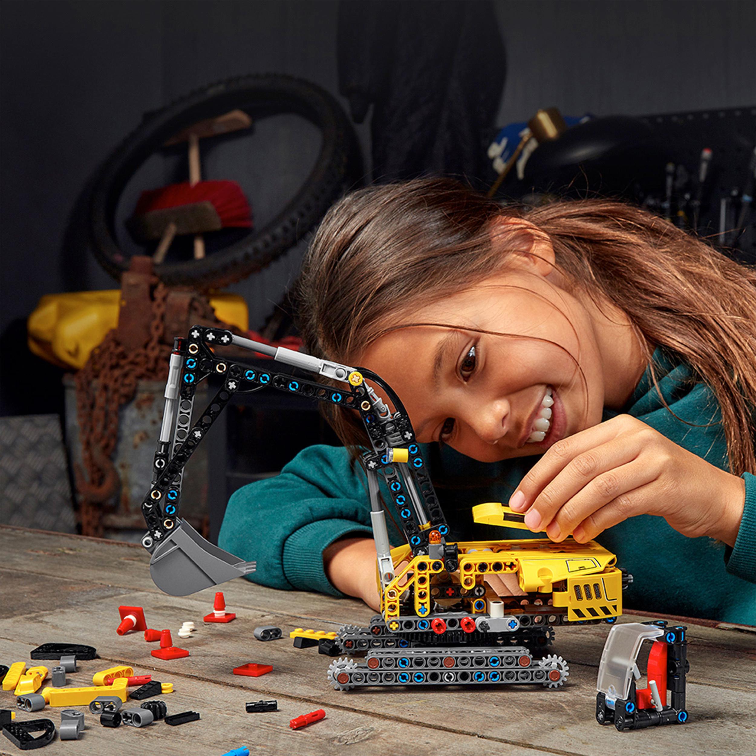 Child building a LEGO® Technic Heavy-Duty Excavator model with colorful pieces on a workbench.