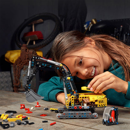 Child building a LEGO® Technic Heavy-Duty Excavator model with colorful pieces on a workbench.