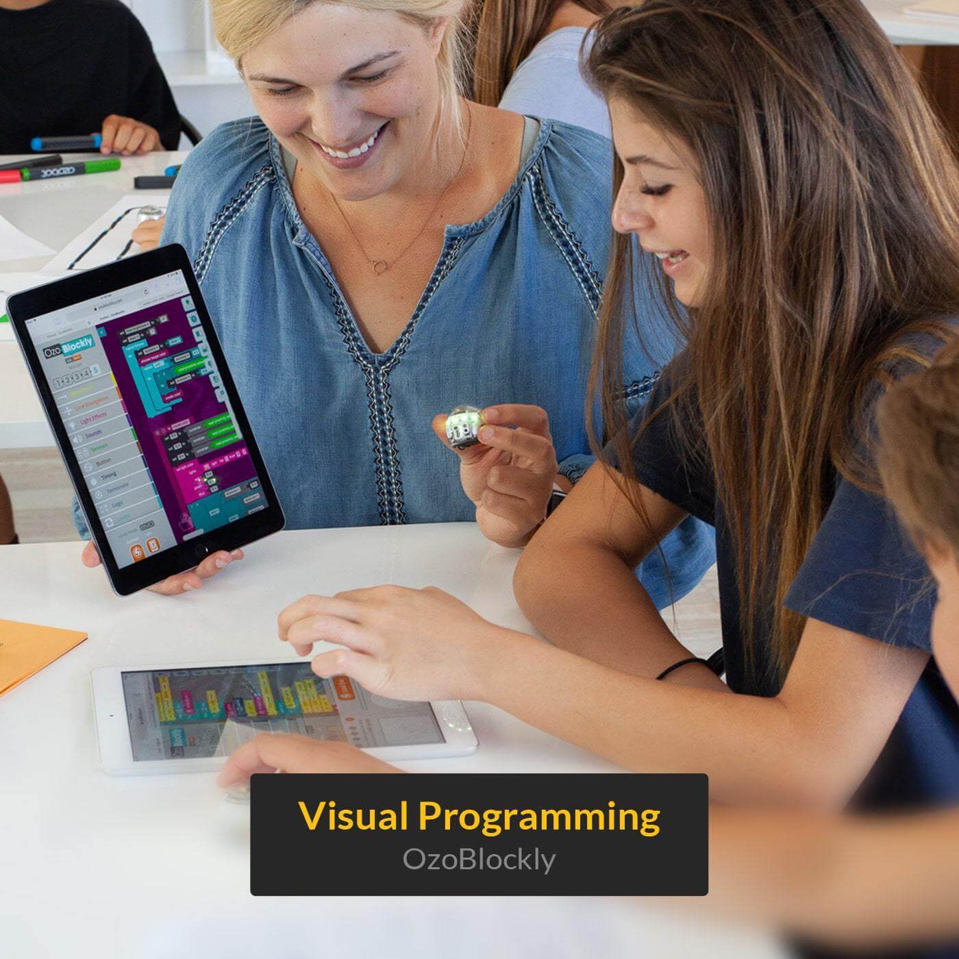 Students enjoying visual programming with Ozobot Evo and OzoBlockly tablet interface in a classroom setting.
