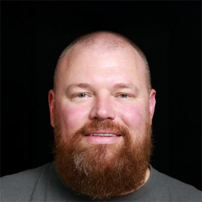 Portrait of a man with a thick beard and short hair against a black background.