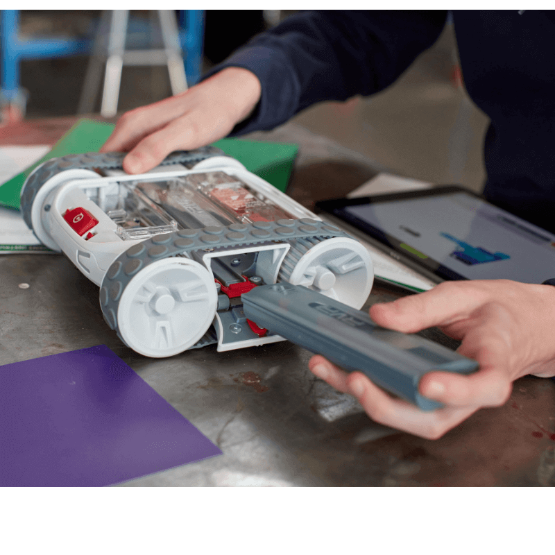 User interacting with Sphero RVR+, plugging in a component on a workbench.