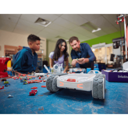 Three students engage with Sphero RVR+ robot in a classroom filled with robotics materials and tools.