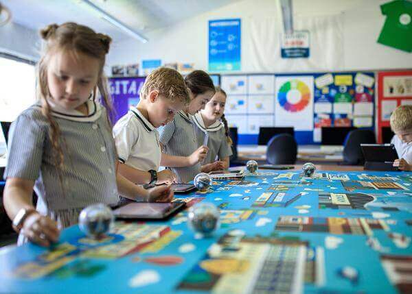 Students engaging in interactive learning activity at a colorful classroom table, using tablets and tools.