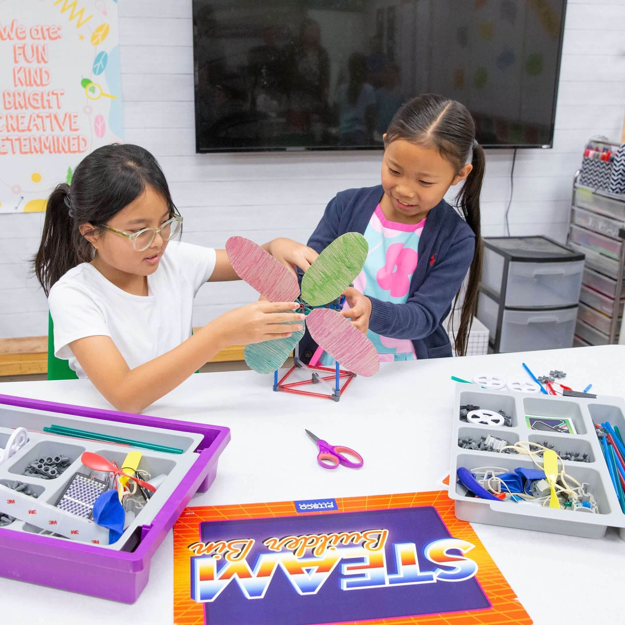 Two children engaging in creative play with the STEAM Builder Bin, designing a model using colorful materials and tools.