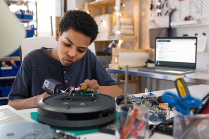 A young boy assembling the Create 3 educational robot, surrounded by tools and a laptop for programming.